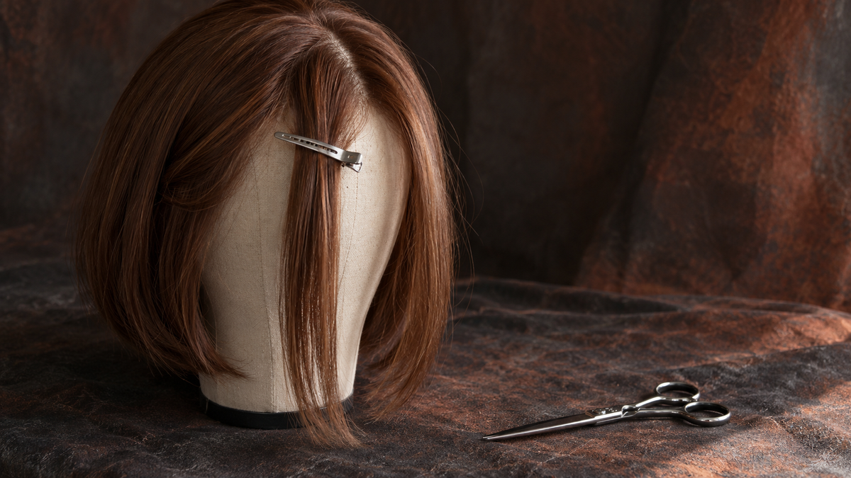Editorial illustration of an auburn bob wig with a long clipped front section and closed hair shears